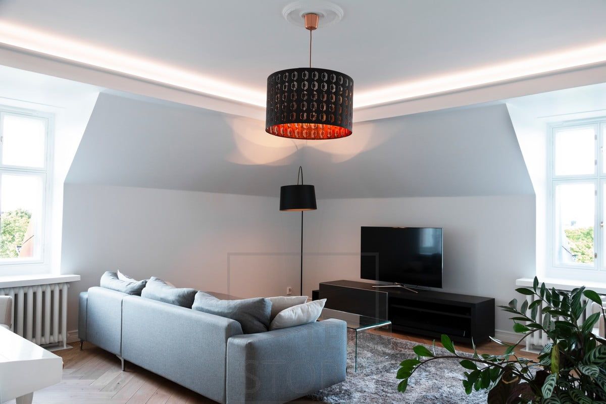 In the living room, a ceiling-mounted baffle with indirect lighting directed at the ceiling. The lighting is atmospheric and soft, without glare.